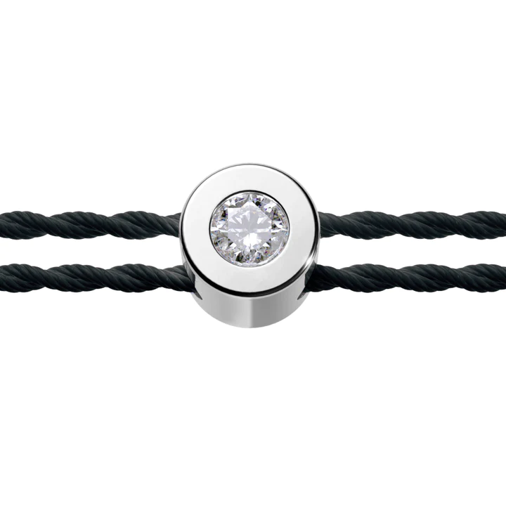 Tête de bracelet ronde et argentée avec un diamant en son centre. Montant noir et fond blanc.