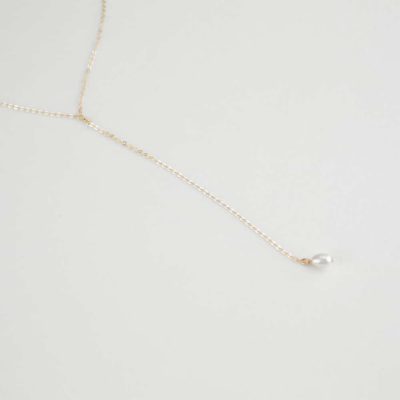 Collier fin couleur or avec une perle au bout sur fond blanc.