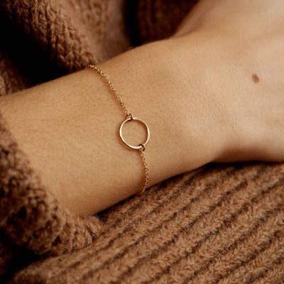 Poignée portant un bracelet en or avec un cercle au centre. En fond on voit un pull marron.