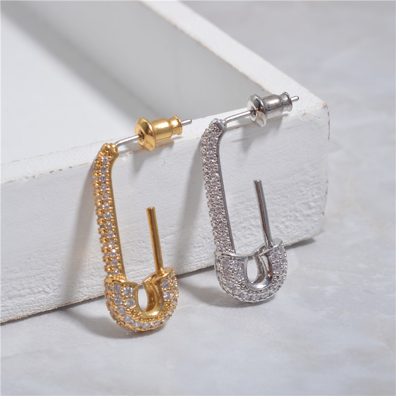 2 boucle d'oreille or et argent en forme de trombone avec des brillants, posées sur un support blanc.