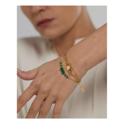 Bracelet multi rang vert et doré porté par une femme qui montre son poignet. Elle porte une chemise blanche.,