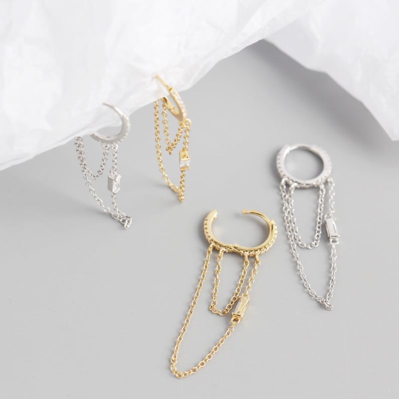 2 paires de boucles d'oreille pendantes. Elles sont posées ou accrochées à un papier blanc. Elles sont couleur or et argent.